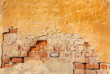 Wall texture with yellow ochre plaster and peeling bottom with exposed brick. Wall background with...