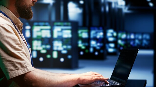 System administator using laptop to audit server mainframes with high computing power, enabling high tech facility to support demanding applications such as machine learning and 3D rendering workloads