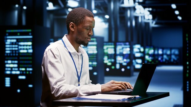 Computer scientist using laptop to debug servers cabinets helping companies manage databases, host websites and store files. Repairman reviewing high tech facility used for high performance computing
