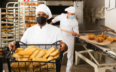 male baker in mask with sesame bread in black box in kitchen