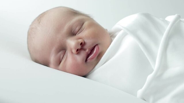 A 3-day-old baby wrapped in white cloth sleeping on a white background.