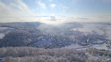 AERIAL: Charming village covered with fresh snow revealing under misty clouds