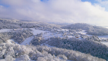 Fototapeta na wymiar AERIAL: A cute little village on a hill covered with a fresh winter blanket