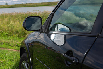 Fototapeta na wymiar Side rear view mirror on a modern black car outdoor. Close-up of automobile detail