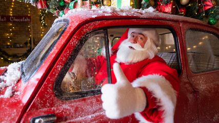 Portrait of Santa Claus driving a red car at Christmas and showing thumbs up. 