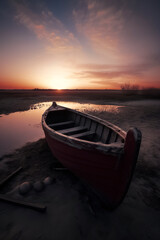 red boat on a beach at sunrise, with the sun casting a beautiful orange and pink glow in the sky, ai generative