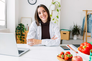 Portrait of young beautiful nutritionist woman smiling at camera at medical consultation. Professional healthcare worker concept