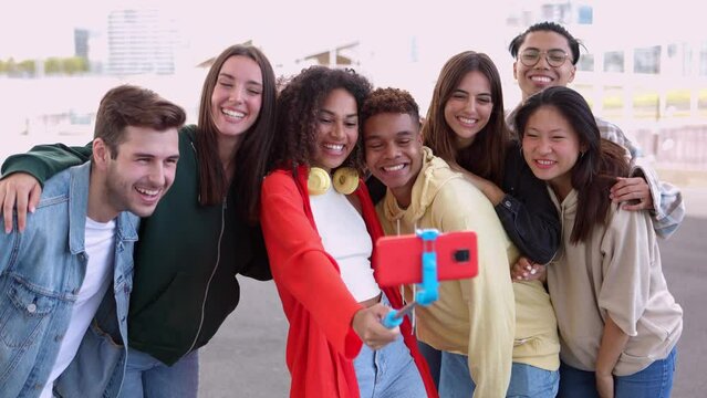 Happy young group of multiracial friends taking self portrait with selfie stick. Diverse student people having fun together posing for photo enjoying free time outdoors. Friendship and youth concept