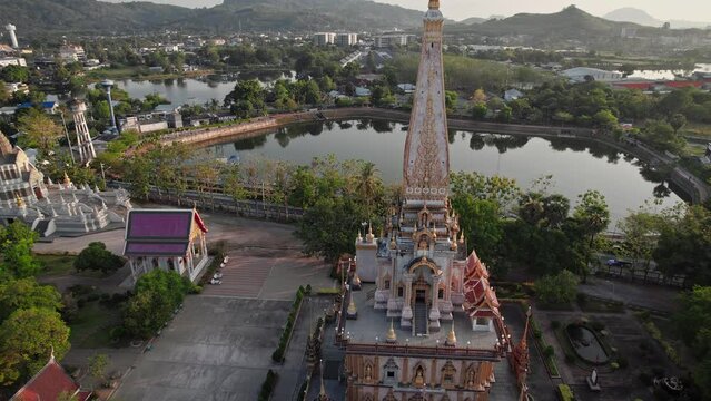 Beautiful buddhist temple at Phuket town, Thailand with a lake and lush jungle hills in the background. Aerial drone footage during sunrise in the morning. Wat Chalong