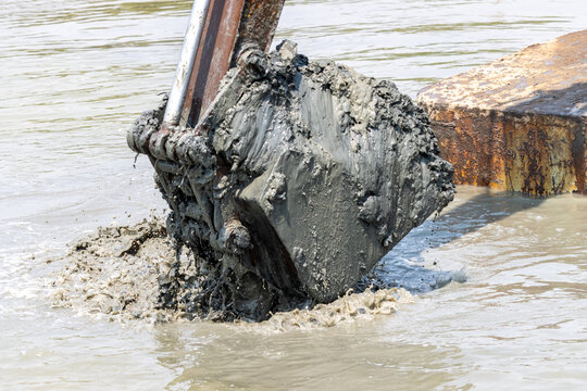 Dredging the bottom of water area, view of the bucket of the floating excavator full of mud