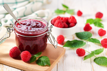 Homemade raspberry confiture in a jar on a white wooden table. Delicious homemade natural raspberry jam.