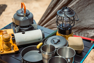Camping essentials neatly arranged at a beachfront tent, kettle, pot, pan, gas stove, flashlight,...
