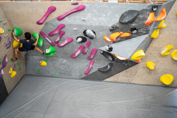 Young Man Climbs Training Wall at Sports Center. Strong Experienced Rock Climber Practicing Solo Climbing on Bouldering Wall in Gym. Man Exercising at Indoor Fitness Facility. Shot from Back