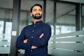 Confident bearded Indian business man leader looking away standing in office hallway. Professional...