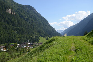 Panoramic view of a bench in the Kaunertal valley in a sunny august day, on the background the Feichten town and the austrian alps