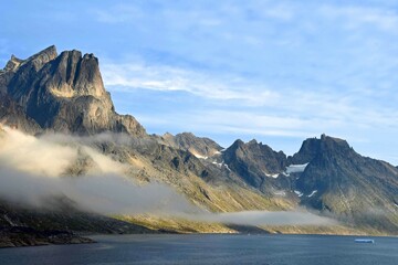 Fototapeta na wymiar the steep, glaciated granite peaks of the western side of the prince christian sound and wisps of fog, in southern greenland, from a cruise ship