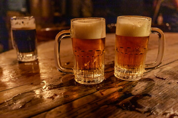 Mugs with pilsner beer in a wood table in a pub.