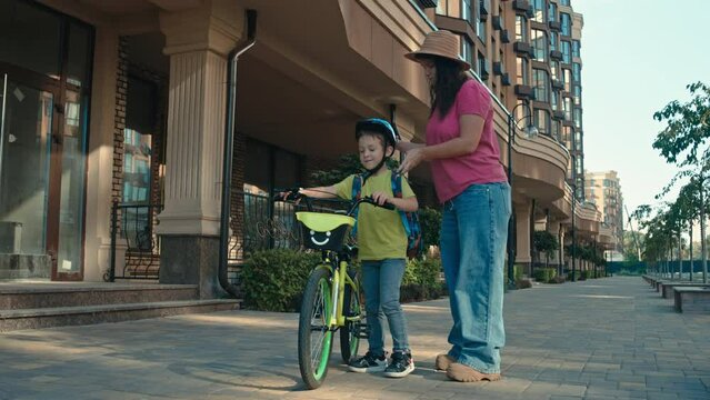 Mother puts on her son's school backpack. The boy goes to school on a bicycle smiling. The child is in a hurry for lessons. parents and children. High quality 4k footage
