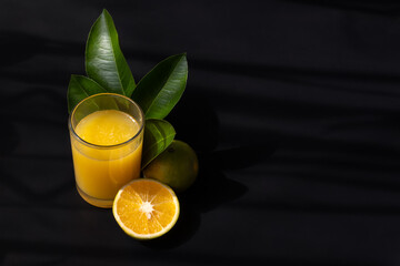 Orange juice, leaves and fruit with a black background and space for text on the right side
