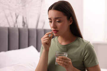 Depressed woman with glass of water taking antidepressant pill on bed indoors, space for text