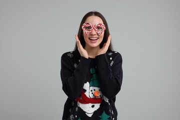 Happy young woman in Christmas sweater and funny glasses on grey background