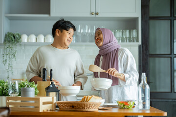Fototapeta na wymiar Cute son And His Muslim Mom In Hijab Preparing Pastry For Cookies In Kitchen, Baking Together At Home. Islamic Lady With son Enjoying Doing Homemade Pastry, preparing to cook breakfast for her family.