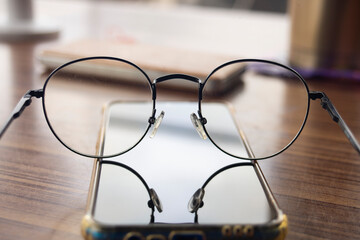 Smartphone and eyeglasses on the wooden table in the office