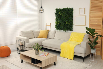 Green artificial plant wall panel and comfortable furniture in cozy living room. Interior design