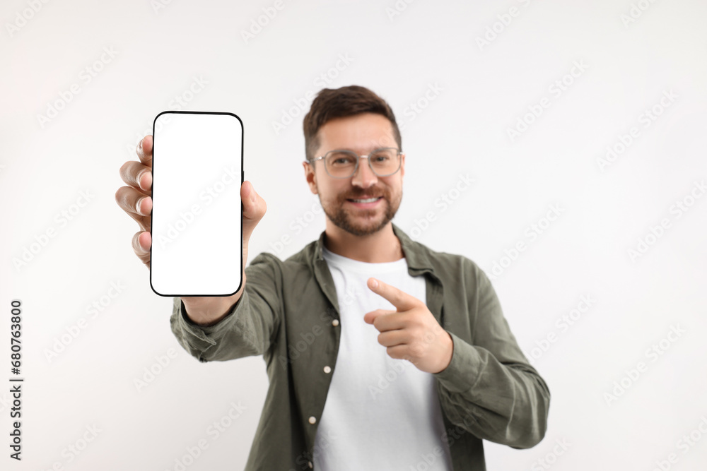 Wall mural Handsome man showing smartphone in hand and pointing at it on white background, selective focus. Mockup for design