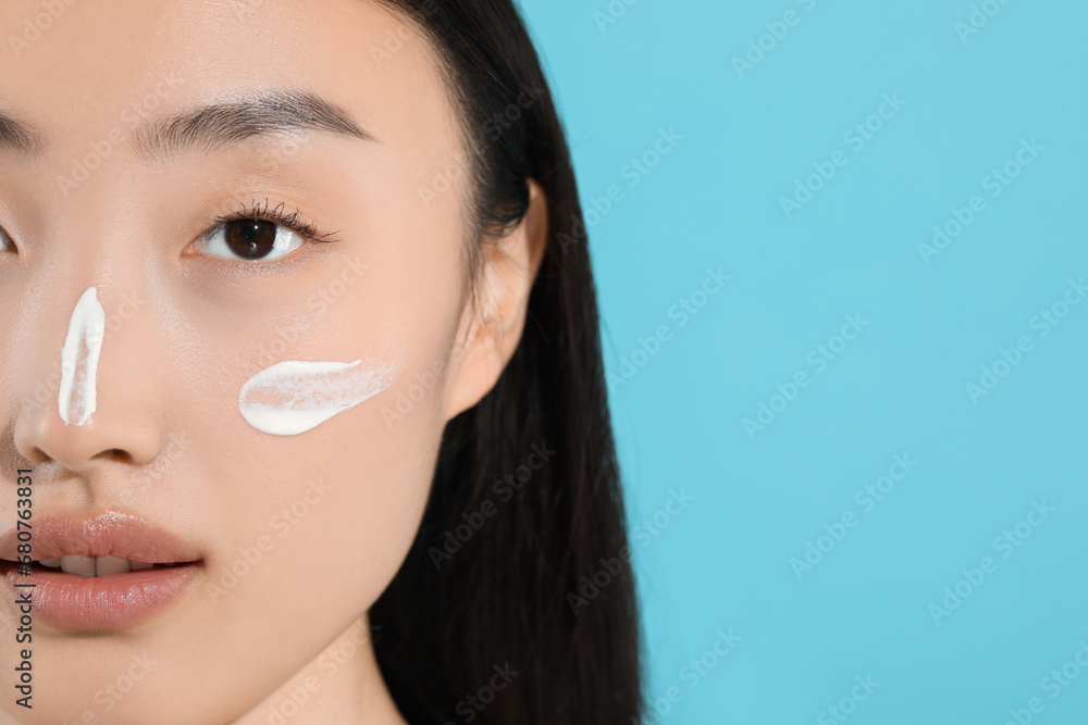 Canvas Prints Beautiful young woman with sun protection cream on her face against light blue background, closeup. Space for text