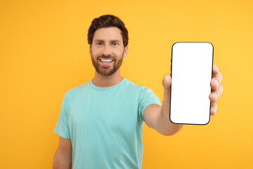 Handsome man showing smartphone in hand on yellow background, selective focus. Mockup for design - obrazy, fototapety, plakaty