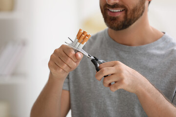 Stop smoking concept. Man cutting cigarettes on blurred background, closeup
