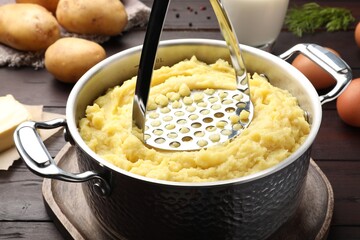 Mashing potatoes in pot on wooden table, closeup