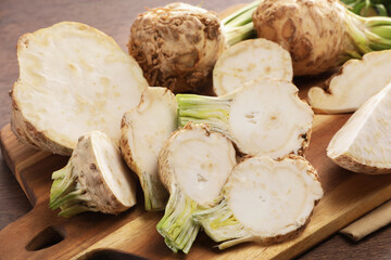 Whole and cut celery roots on wooden table, closeup