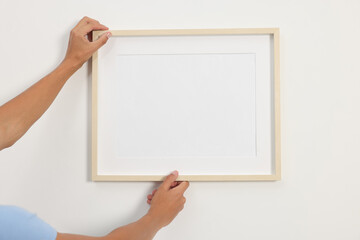 Obraz premium Young man hanging picture frame on white wall indoors, closeup