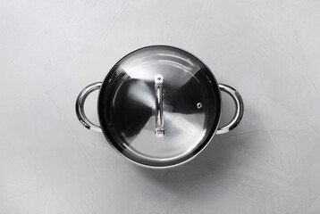 One steel pot with glass lid on light textured table, top view