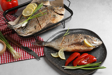 Delicious baked fish served with green onion, bell pepper and lemon on light textured table. Seafood