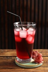 Glass of delicious iced hibiscus tea with straw and dry flowers on wooden table