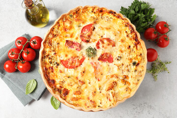 Tasty quiche with tomatoes and cheese served on light table, flat lay