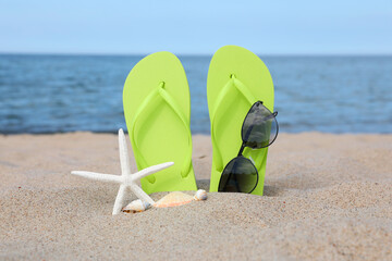 Stylish light green flip flops, sunglasses, starfish and seashells on beach sand