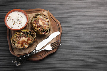 Tasty grilled artichoke and sauce on dark wooden table, top view. Space for text