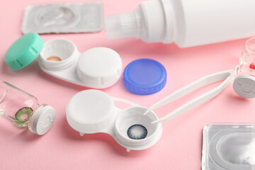 Cases with color contact lenses, bottles of solution and tweezers on pink background