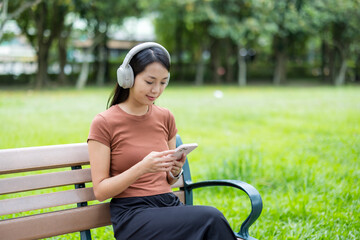 Obraz premium Woman listen to headphone and use of cellphone at park