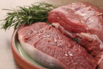 Pieces of raw beef meat with spices and rosemary on table, closeup