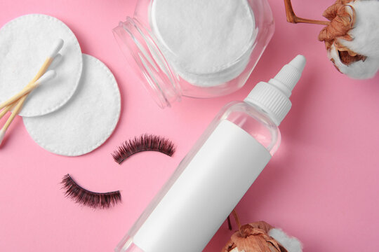 Bottle of makeup remover, cotton flowers, pads, swabs and false eyelashes on pink background, flat lay