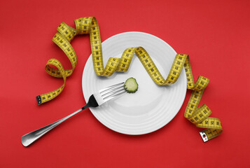 Plate with cucumber slice, measuring tape and fork on red background, top view. Diet concept - obrazy, fototapety, plakaty