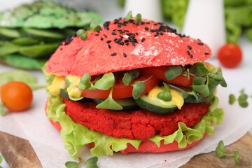 Tasty pink vegan burger with vegetables, patty and microgreens on wooden table, closeup