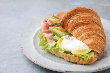Delicious croissant with prosciutto, avocado and egg on grey table, closeup. Space for text