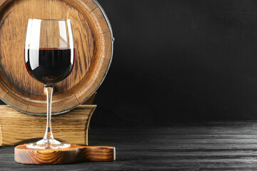 Wooden barrel and glass with delicious wine on black table, space for text