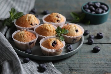 Delicious sweet muffins with blueberries and mint on light blue wooden table